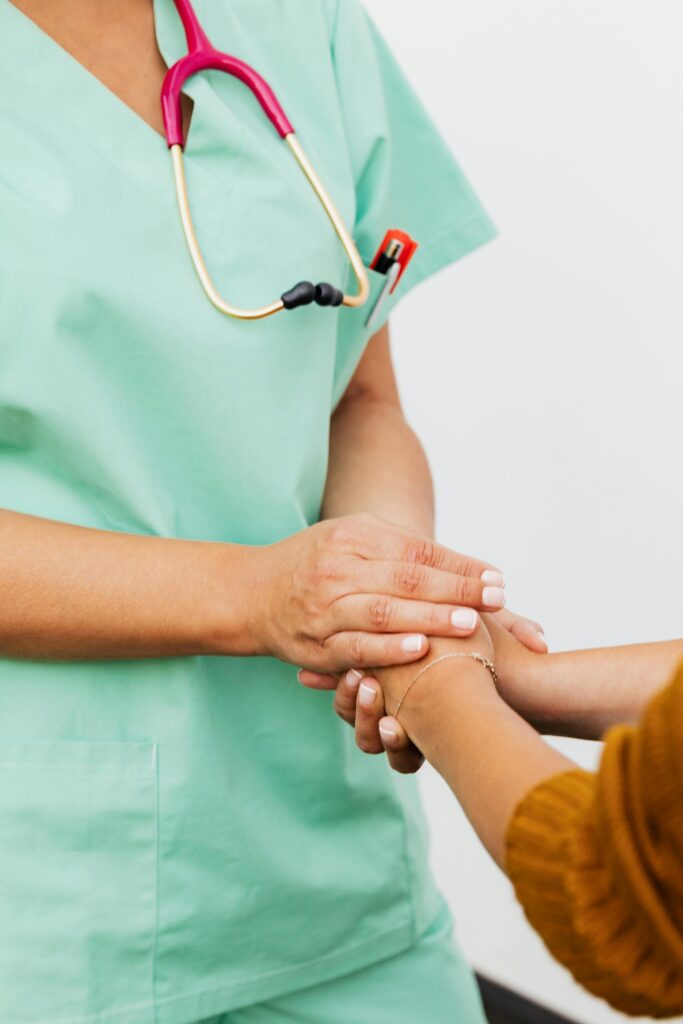 A nurse in green scrubs gently clasps a patient's hand, offering support.