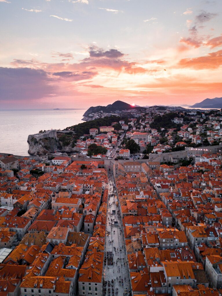 Stunning aerial view of Dubrovnik's Old Town with red rooftops and sunset sky over the Adriatic Sea.