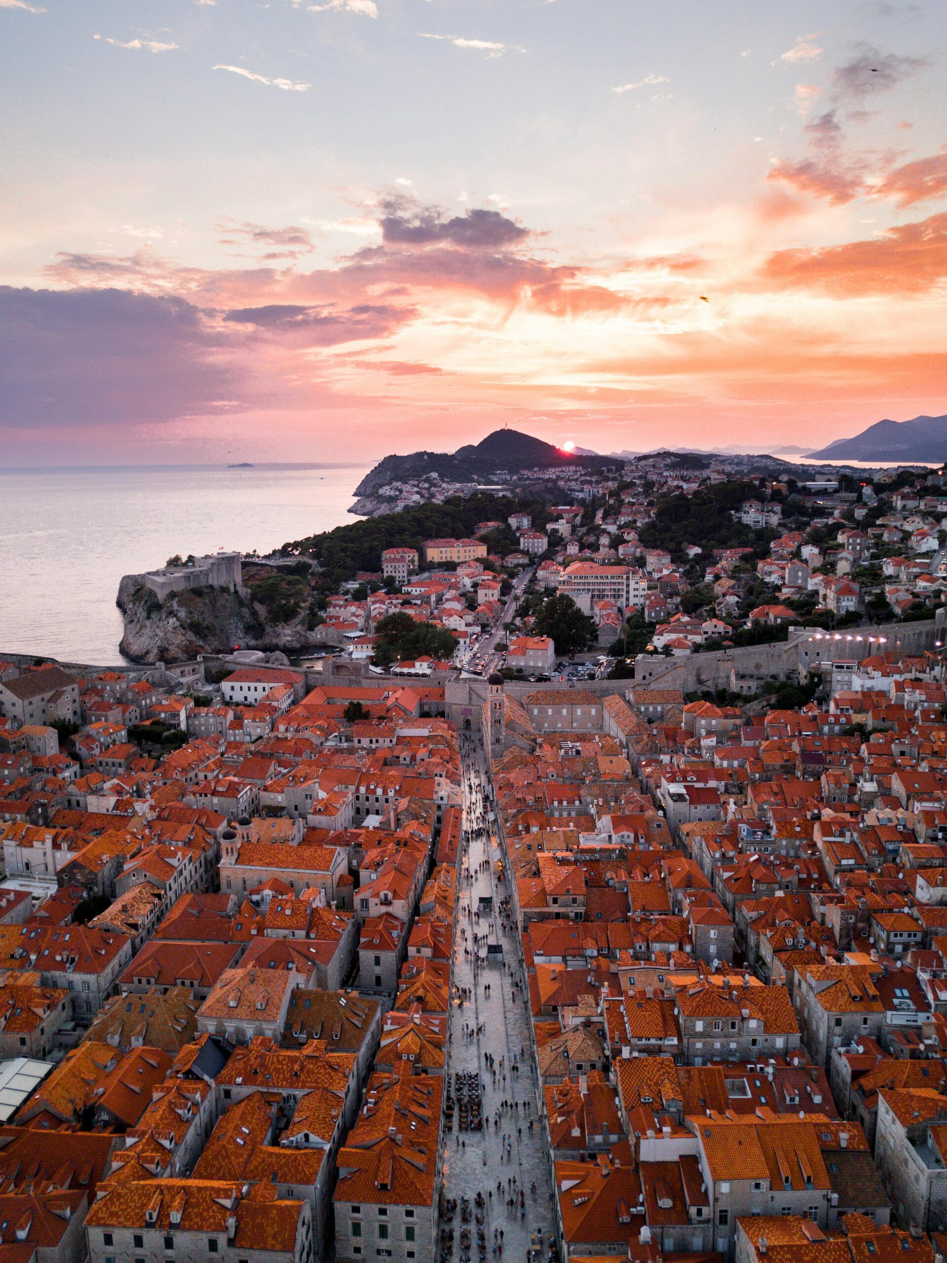 Stunning aerial view of Dubrovnik's Old Town with red rooftops and sunset sky over the Adriatic Sea.
