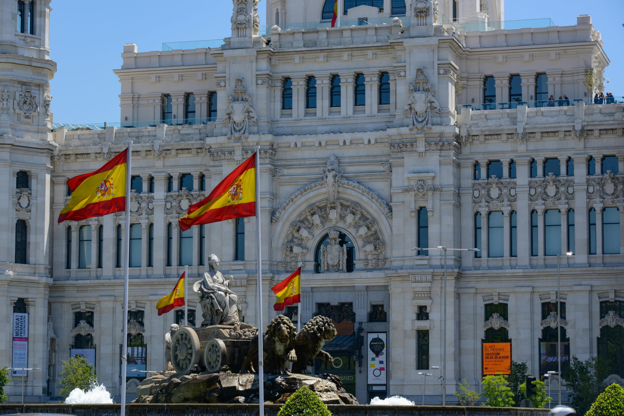 Cybele Palace in Madrid adorned with flying Spanish flags and a stunning fountain.
