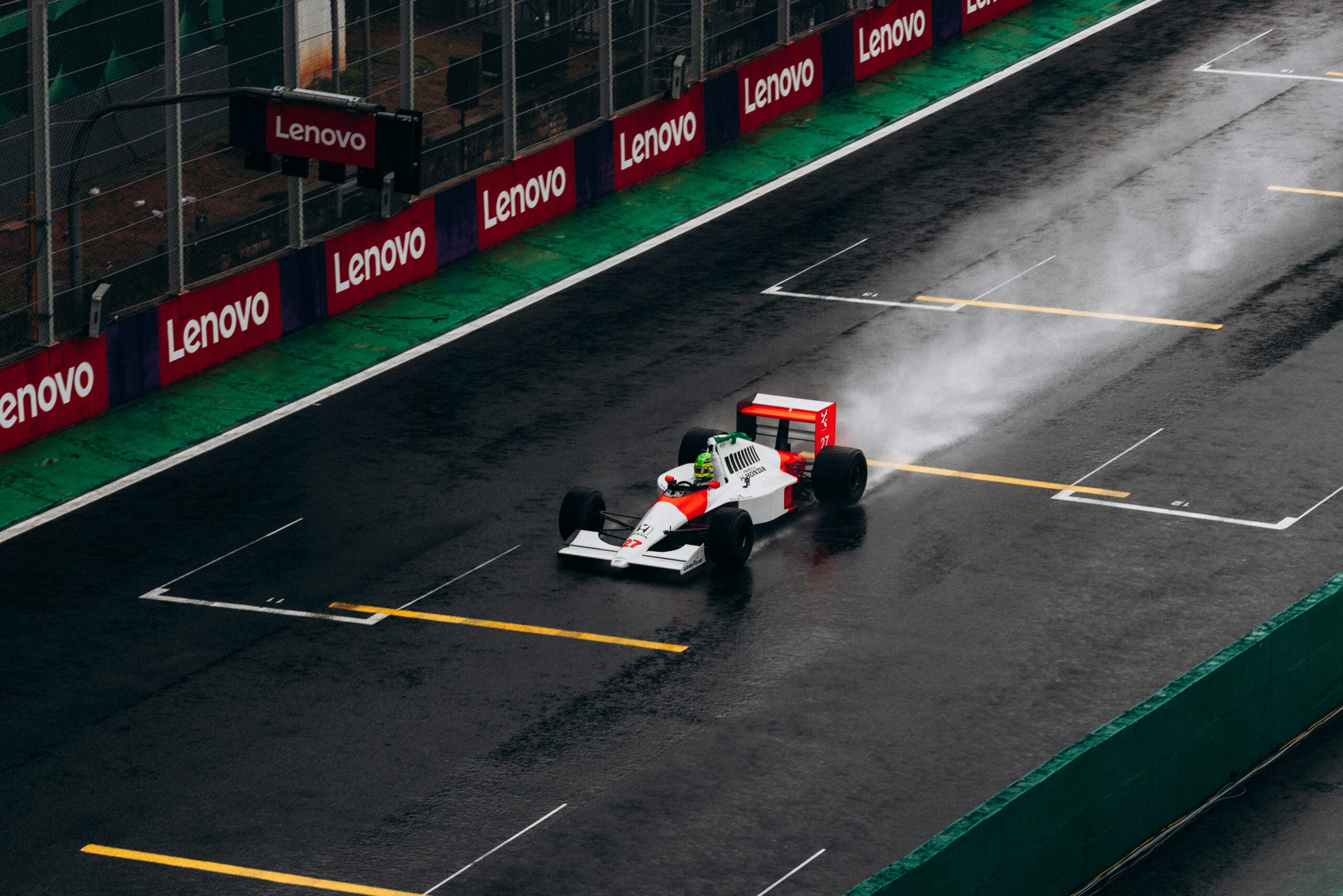 A classic Formula 1 car races on a wet track at Interlagos, Brazil, leaving a trail of spray behind.
